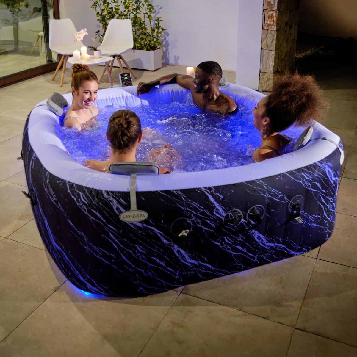 Grupa ludzi relaksujących się w dmuchanym jacuzzi Lay-Z-Spa Hollywood na tarasie z włączony niebieskim podświetleniem LED.